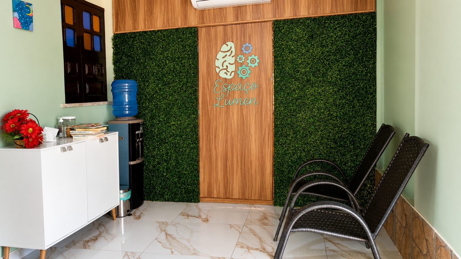 Recepção do Espaço Lumen, com parede verde, porta de madeira e poltronas