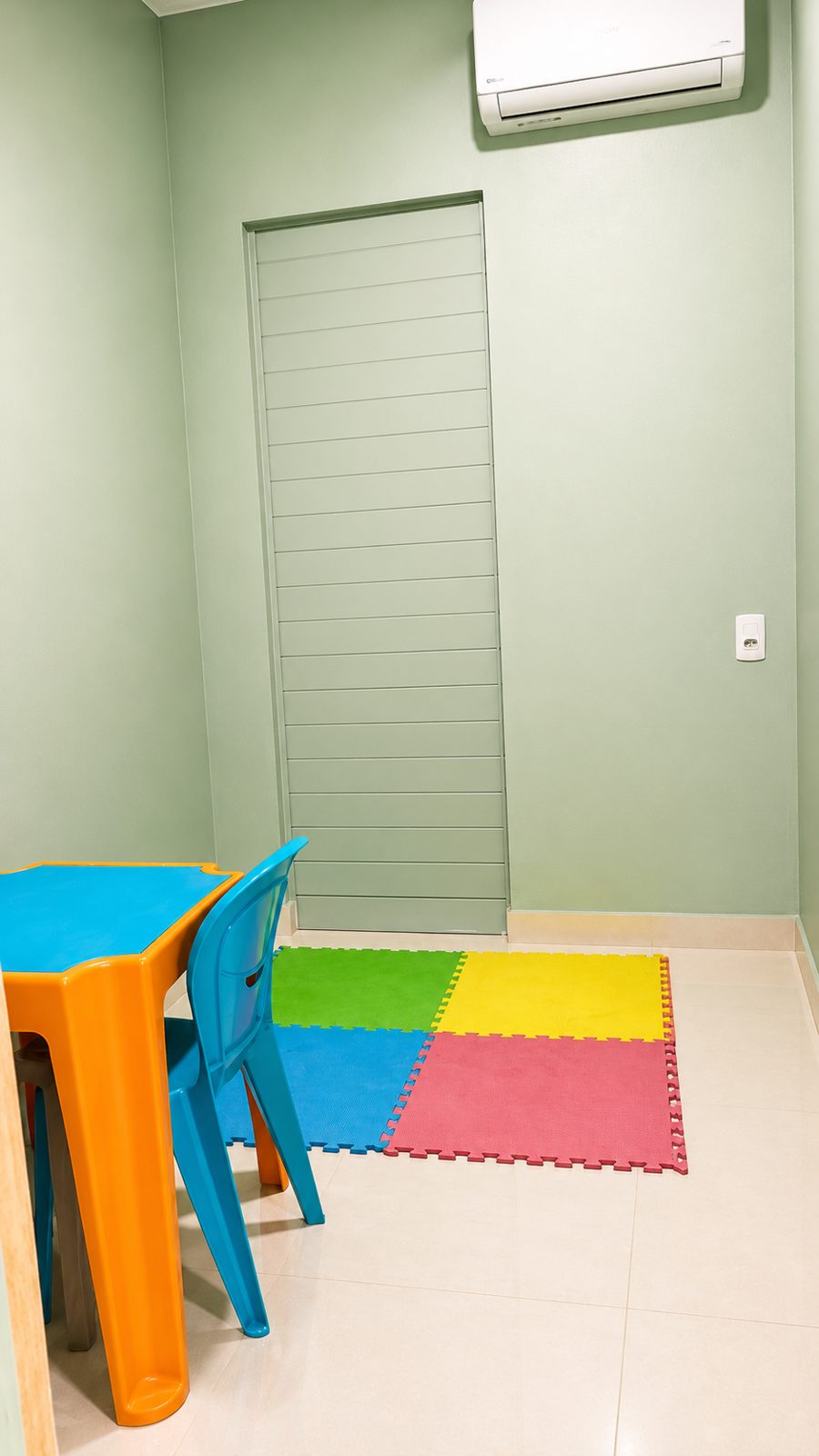 Sala infantil com mesinha laranja, cadeira azul e tapete colorido